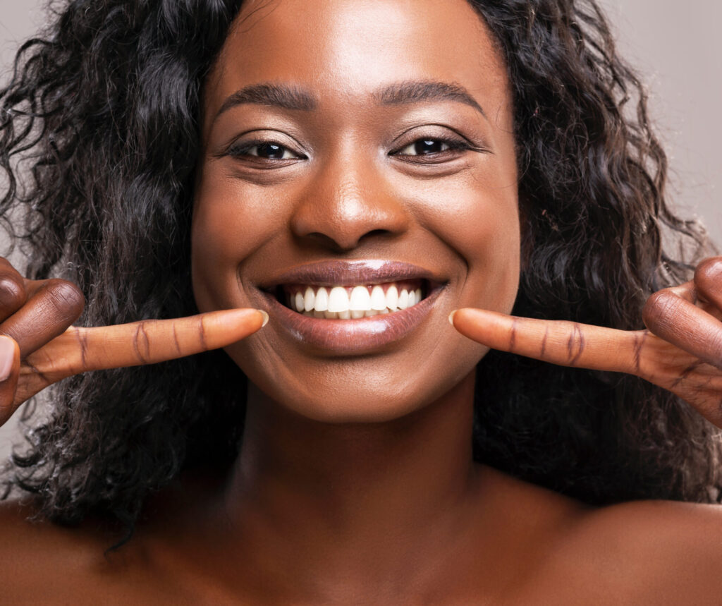 Happy black woman pointing at her perfect white teeth